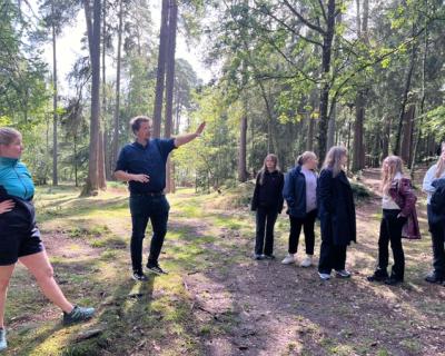 Læreren står ute i skogen og peker. 