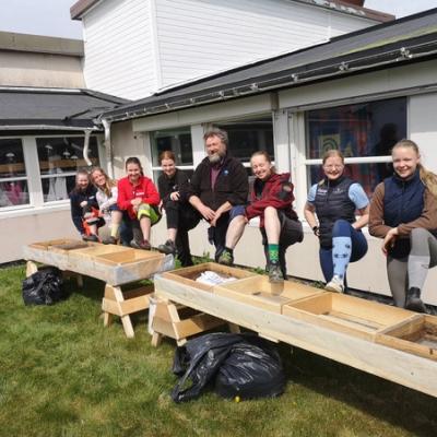 Jørgen og elevene med en fot hver oppå vekstkassene til skolehagen. 