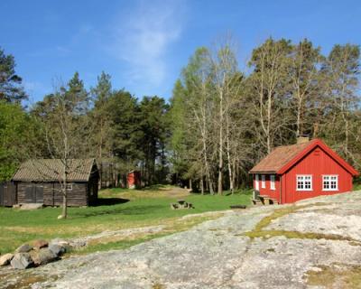 Et lite rødt hus og en brun liten låve på en liten plass i et parkområde.