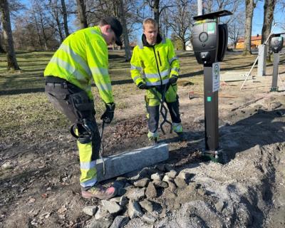 2 elever løfter en granittkantstein på plass ved en ladestasjon.